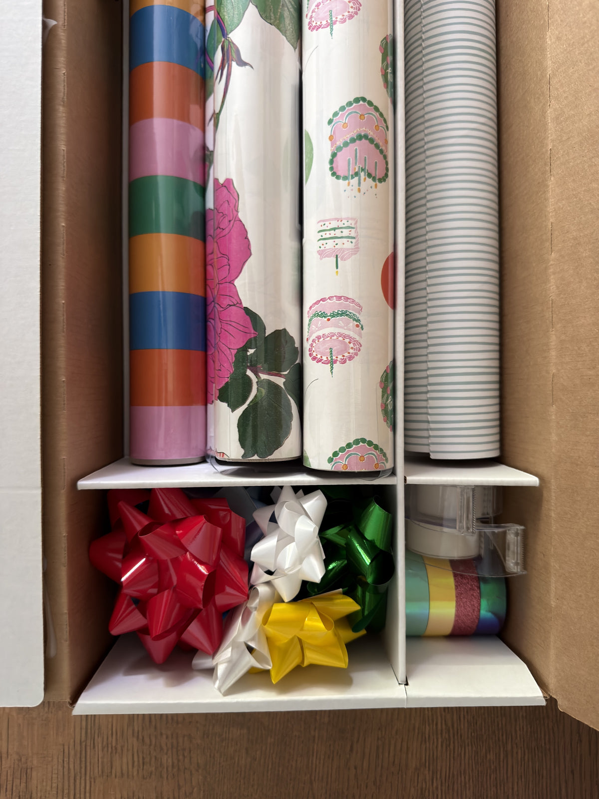 Interior dividers holding rolls upright above compartments for bows, ribbon and tape