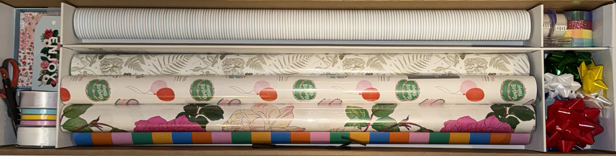 Top-down view of the case loaded with four wrapping paper rolls, ribbon, bows and tape
